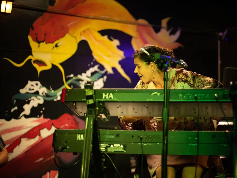 Woman smiling while playing a green keyboard on stage before a colorful fish mural