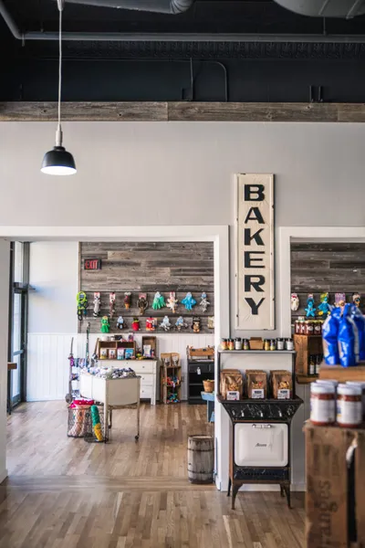 Rustic market interior with a vertical Bakery sign, wood-plank accent wall, vintage stove, and colorful merchandise