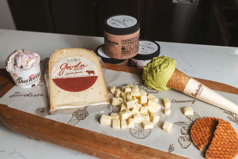 Gouda cheese wedge and cubes, gelato cups, a green-scooped waffle cone, and stroopwafels on a wooden board