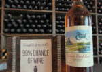 Bottle of rosé wine beside a small book titled '99% Chance of Wine' on a wooden rack