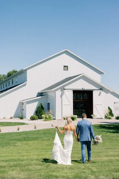 Bride and groom walking hand-in-hand toward a large white barn wedding venue