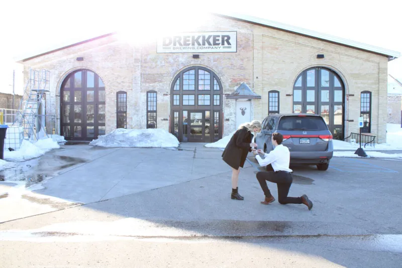 Man on one knee proposing to a woman outside Drekker Brewing Company in winter