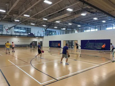 Players competing in pickleball on indoor hardwood courts in a large recreation center