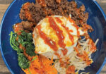 Blue bowl of bibimbap topped with a fried egg and red sauce