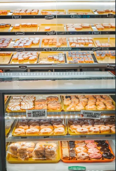 Glass display case filled with rows of assorted donuts including Nutella and caramel apple bismarks