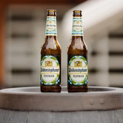 Two Weihenstephaner Festbier bottles standing on a wooden barrel