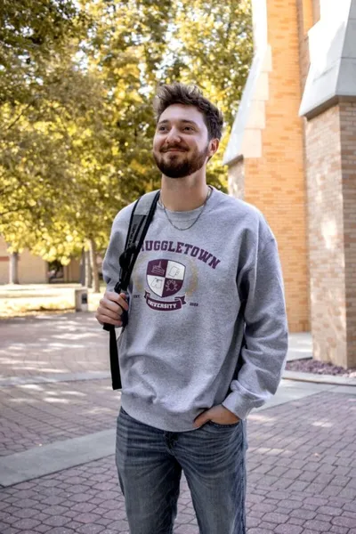 Young bearded man with backpack wearing a gray university sweatshirt on a brick campus path