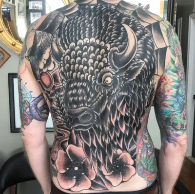 Man's back covered in a large black-and-grey bison head tattoo with flowers