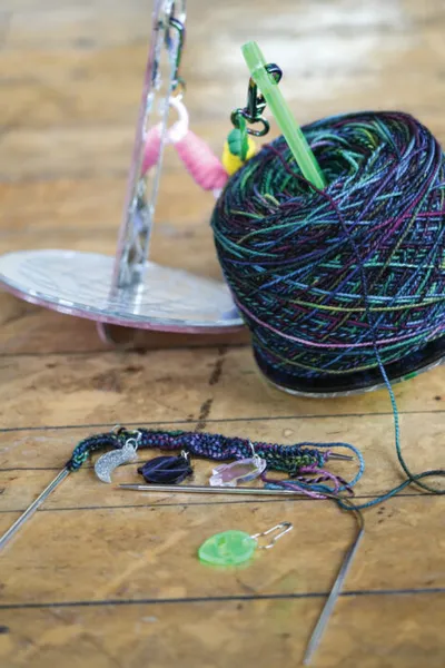 Ball of multicolored yarn with stitch markers and knitting needles on a wooden surface