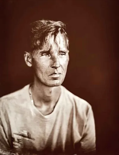 Sepia-toned wet plate portrait of a young man in a white t-shirt against a dark background