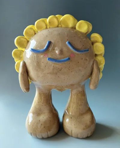 Glazed ceramic figurine with yellow petal crown, closed blue eyes, and rosy cheeks