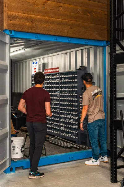 Two men standing at the entrance of a blue shipping container filled with bolt storage racks