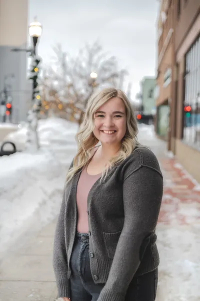 Smiling young woman with blonde hair in a gray cardigan on a snowy downtown sidewalk