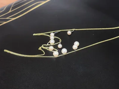 Gold chain necklace with small pearl accents and matching pearl stud earrings on dark surface