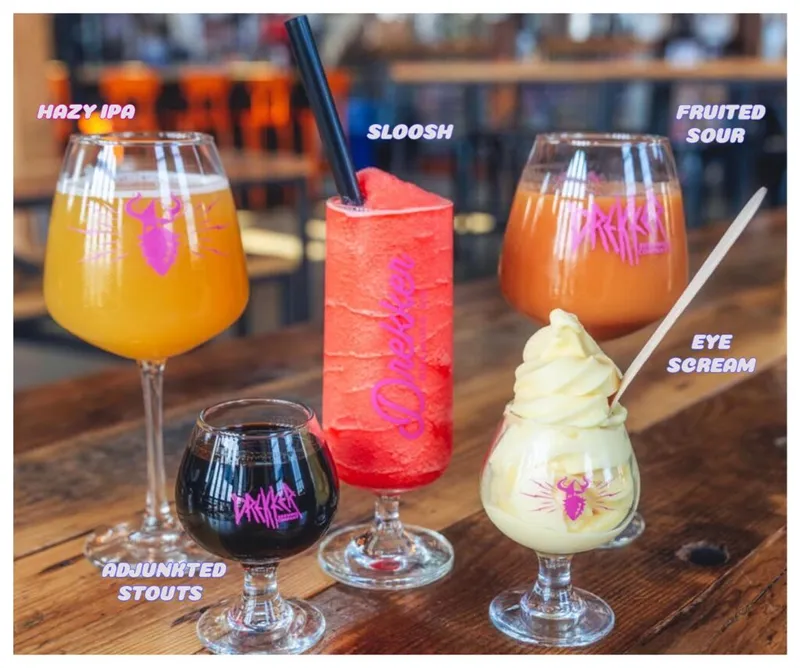 Five branded Drekker drinks on a wood table: hazy IPA, dark stout, red slushy, fruited sour, and ice cream float
