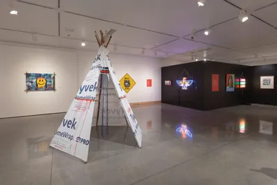 Gallery installation with a Tyvek-wrapped tipi surrounded by neon signs and wall art