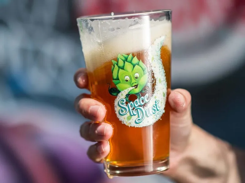 Hand holding a pint glass of amber beer branded Space Dust IPA with a foamy head