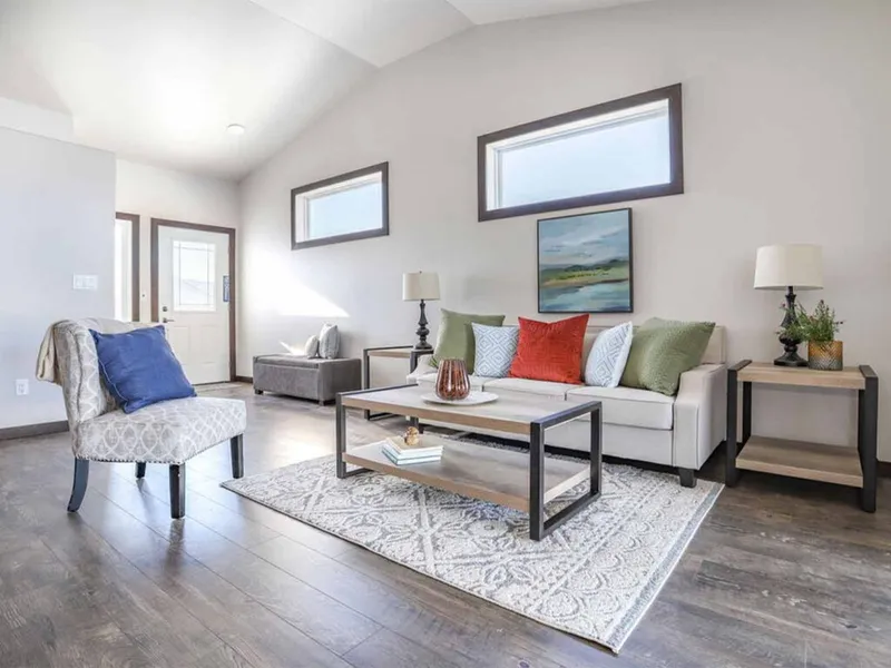Bright living room with gray sofa, colorful pillows, wood coffee table, and dark hardwood floors