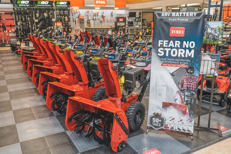 Row of red Toro snow blowers on display inside a hardware store with a Toro banner