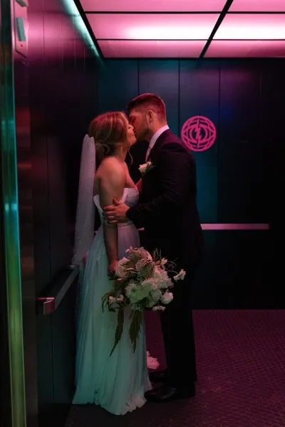 Bride and groom kissing in a dimly lit elevator with pink neon lighting