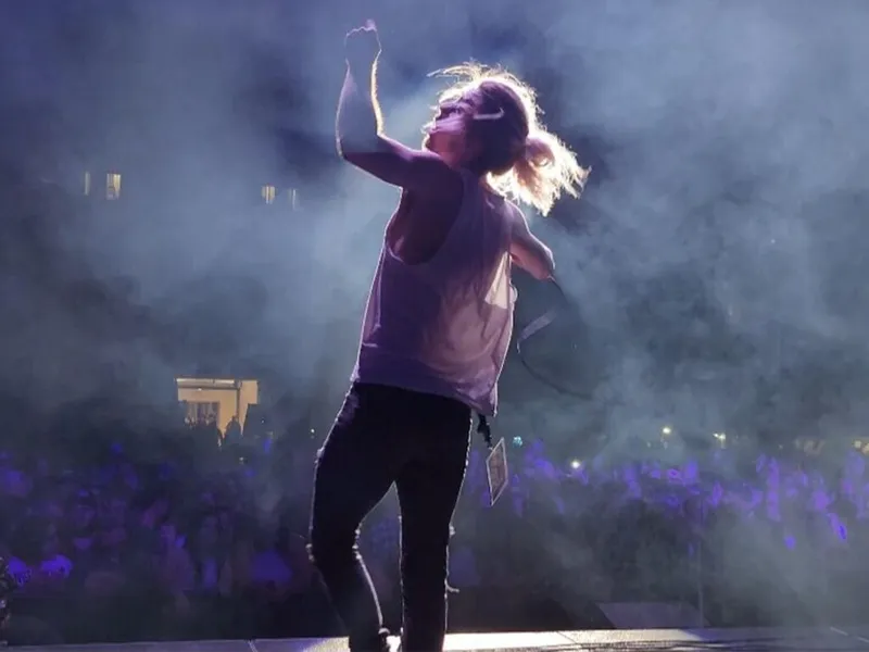 Performer in a purple tank top raises a fist onstage amid dramatic fog and purple stage lighting