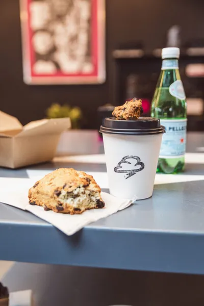 Chocolate chip scone on a napkin beside a branded to-go cup and sparkling water bottle on a gray table