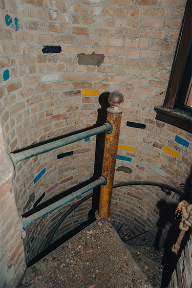 Narrow spiral staircase with rusted newel post and metal railing inside a curved brick tower