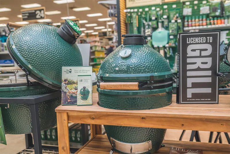 Two green ceramic kamado grills on a wood table in a retail store display