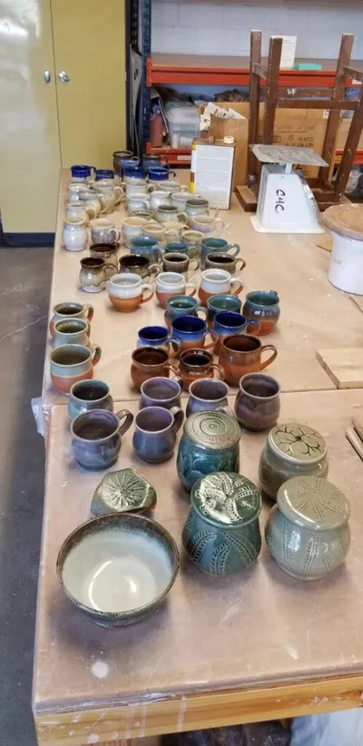 Dozens of handmade ceramic mugs and lidded jars in earthy glazes arranged on a worktable