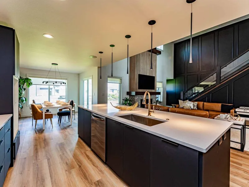 Modern open-concept kitchen with white island, gold faucet, dark cabinetry, and pendant lights