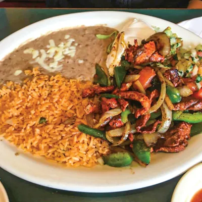 Plate of seasoned meat and peppers stir-fry with Spanish rice and refried beans