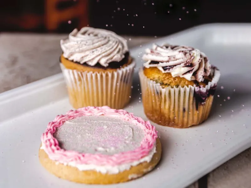 Two frosted cupcakes and a decorated sugar cookie dusted with glitter on a white tray