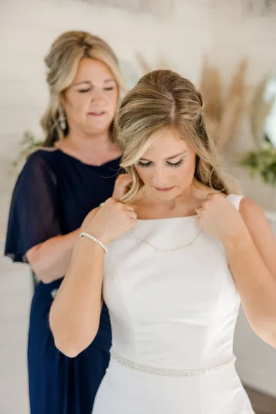 Woman in navy dress fastening a necklace on a bride in a white gown