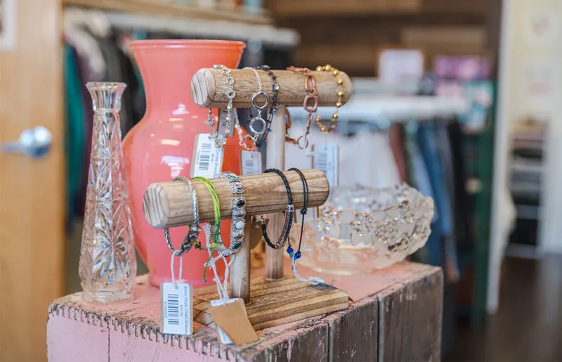 Bracelets and necklaces displayed on wooden jewelry stands beside a coral vase in a boutique