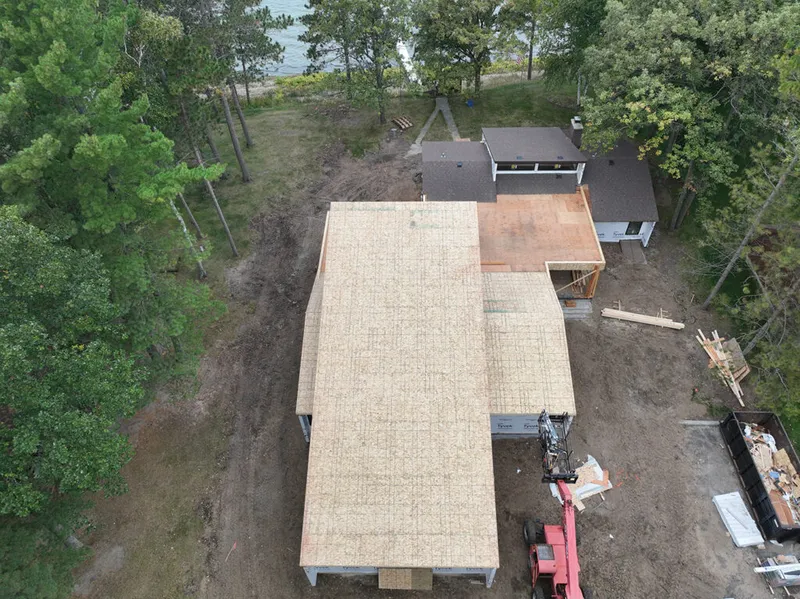 Aerial view of a lakeside home under construction with exposed OSB roof sheathing