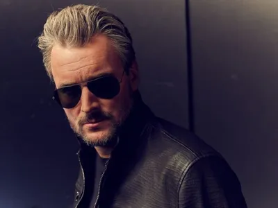 Man with silver swept-back hair and dark sunglasses in a black leather jacket