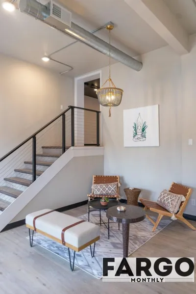 Modern loft lounge with woven chairs, round coffee table, and gold pendant light beneath exposed ductwork