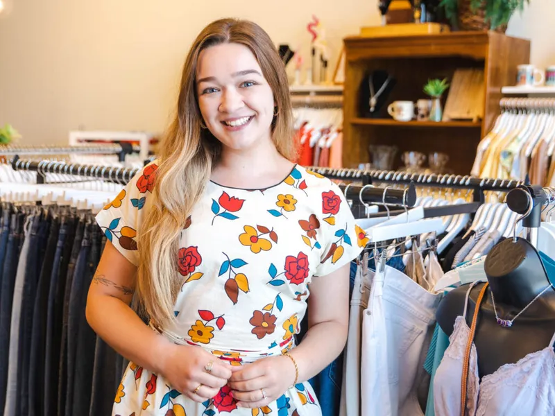Smiling young woman in a floral dress standing among clothing racks in a boutique