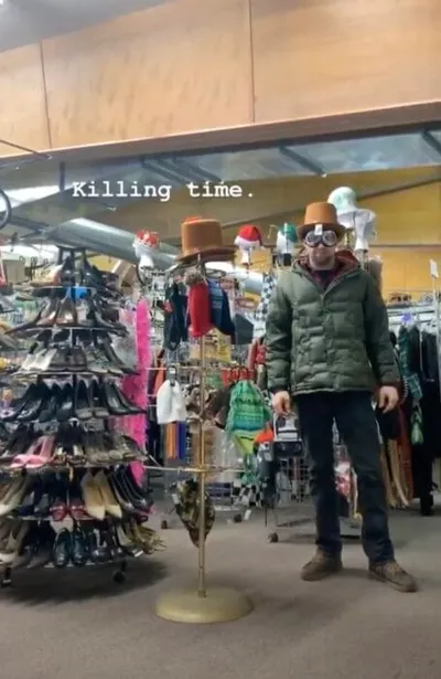 Man wearing novelty goggles and a small top hat inside a cluttered thrift store