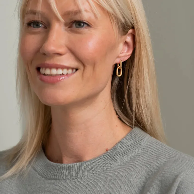 Smiling woman with blonde hair wearing gold chain-link drop earrings and a grey knit top