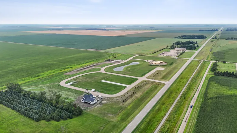 Aerial view of a rural residential development with a small pond, curving drives, and surrounding farmland