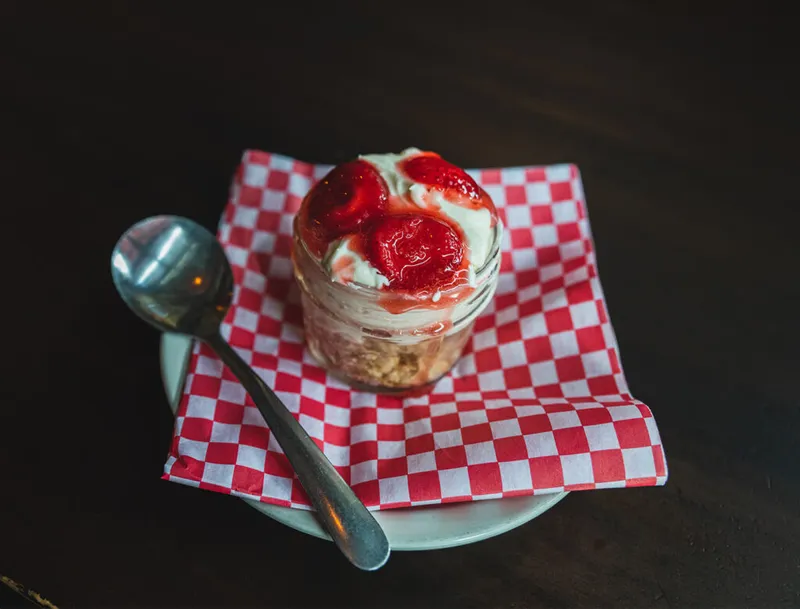 Strawberry shortcake parfait in a jar on a red-checked napkin with a spoon