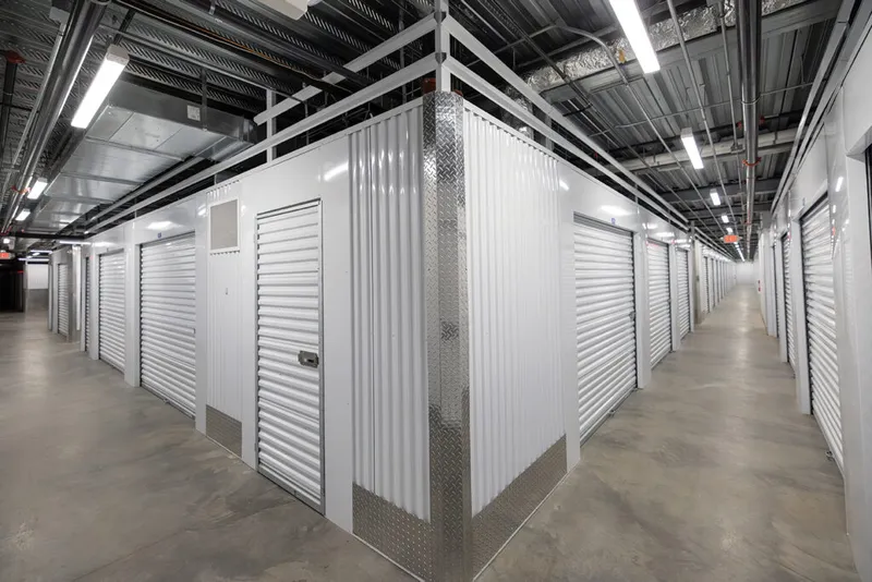 Indoor self-storage hallway lined with white roll-up unit doors on a polished concrete floor
