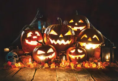 Glowing jack-o'-lanterns grouped on a wooden table with candles and autumn leaves