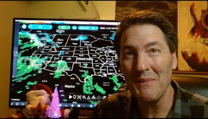 Man smiling in front of a monitor displaying a US weather radar map