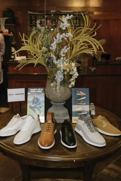 Four dress and casual sneakers arranged on a round wooden table with a floral arrangement and brand signage