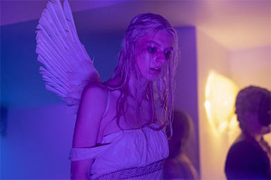 Woman in white angel costume with large wings under purple party lighting