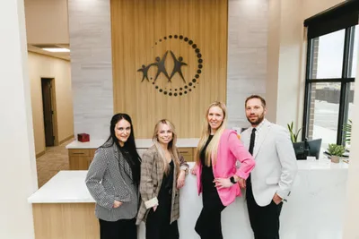 Three women and a man in professional attire posing in a modern clinic lobby with a decorative wall logo