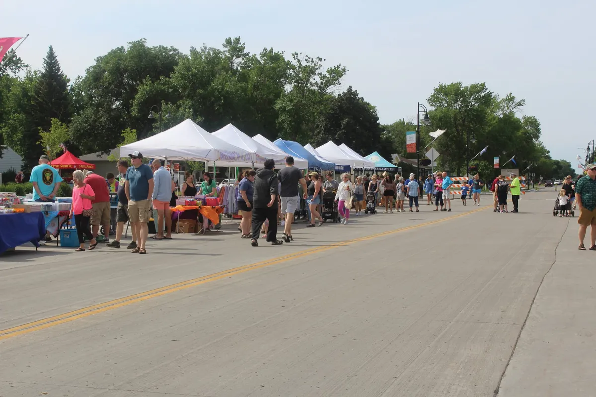 Crowds browse vendor tents lining a closed two-lane street on a sunny summer day