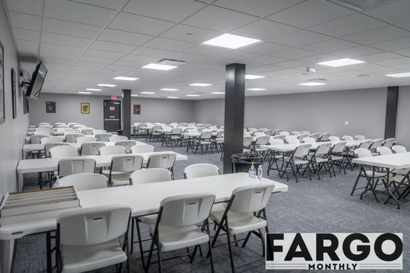 Large empty event room with rows of white folding tables and chairs on gray carpet